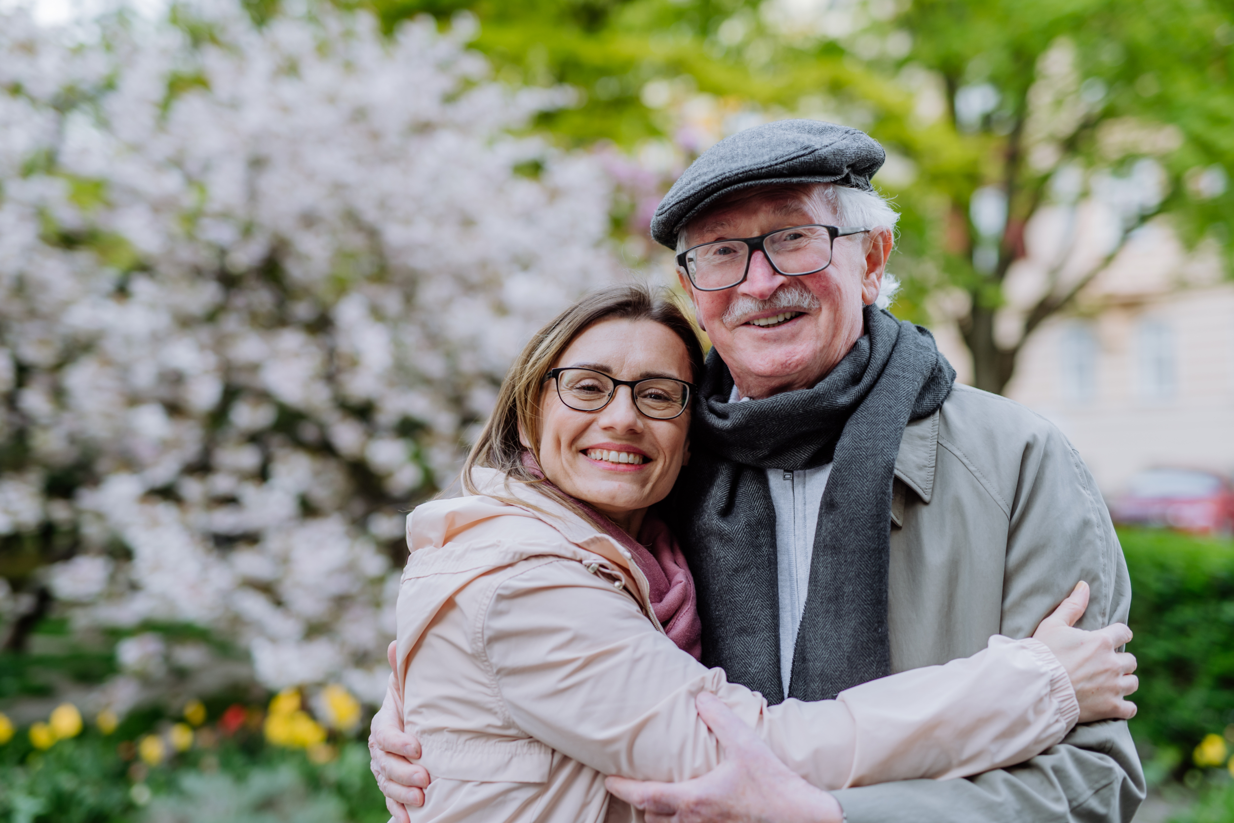 An adult daughter hugging her senior father outdoors in park on spring day before choosing a will writing service